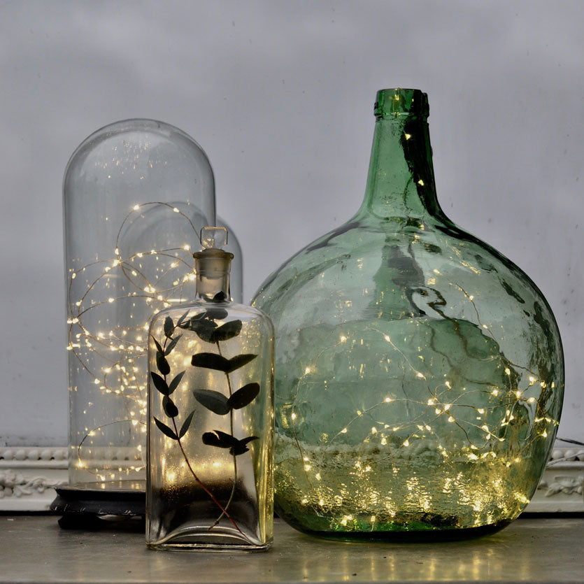 Vintage glass demijohn and other vessels containing warm yellow firefly lights - Christmas home styling ideas from Home Barn